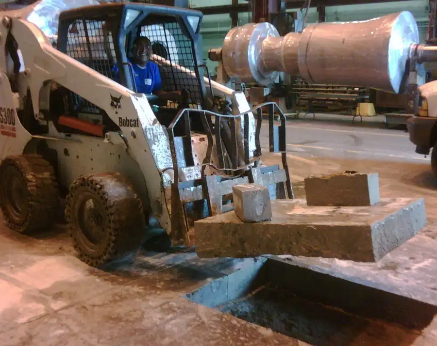 A skid steer lifting cut concrete blocks out of a floor opening inside a plant
