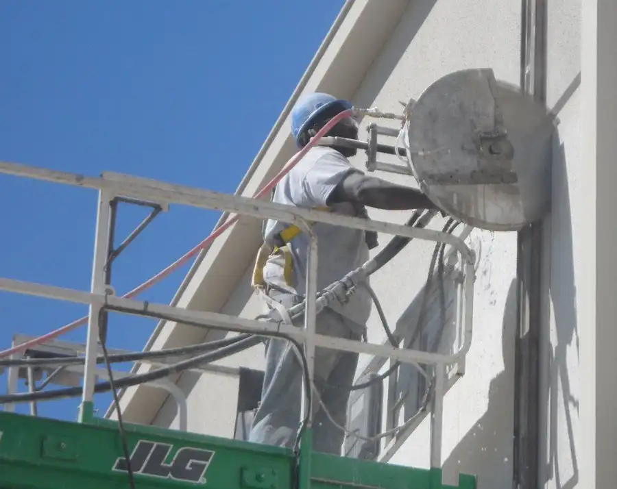 A technician on a boom lift wall-sawing a building facade against open sky