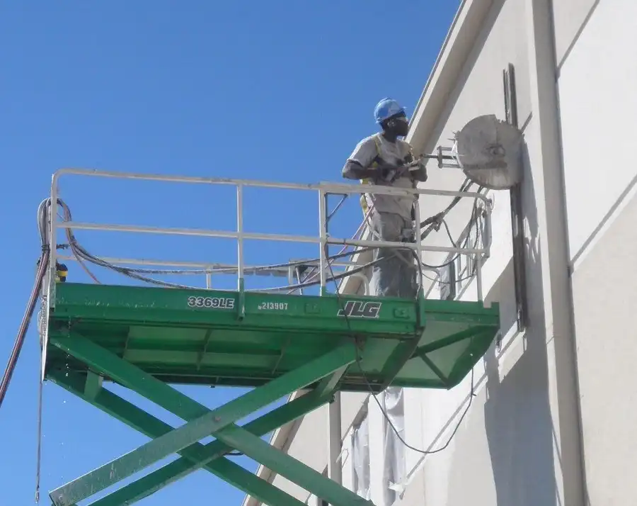 A technician on a scissor lift wall-sawing a tilt-wall panel