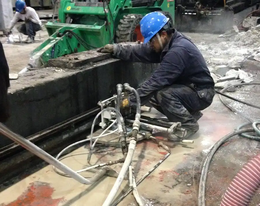 A technician setting a wall saw rail in a pit with a skid steer behind