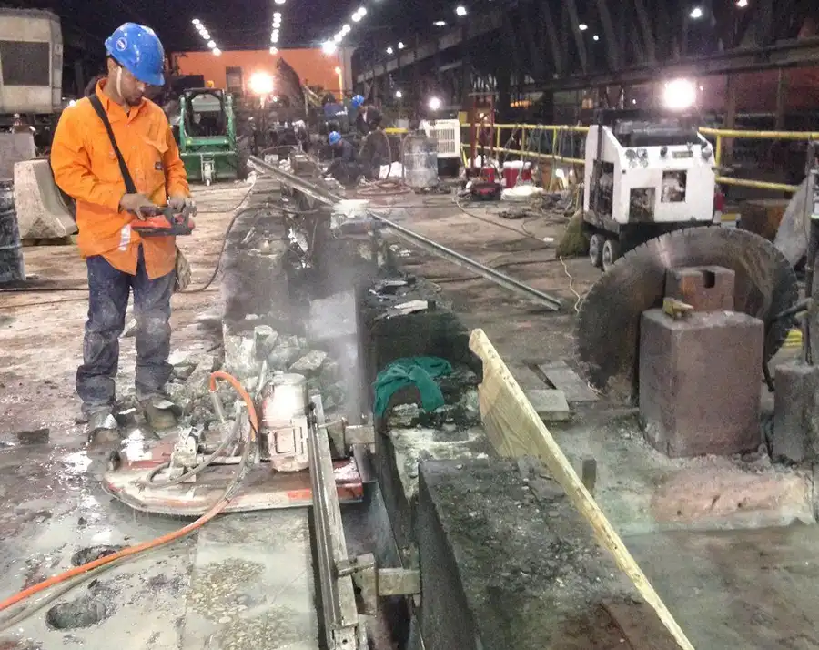 A large-diameter wall saw cutting inside an industrial plant, operator working from a remote pendant