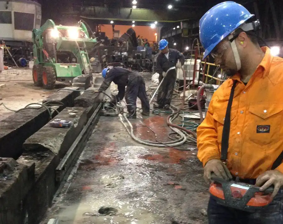 An operator running a wall saw by remote control inside a steel mill