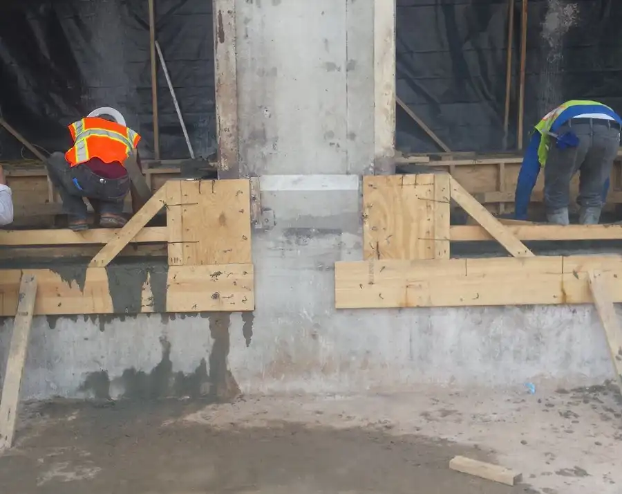 Two Belknap crew members building column formwork behind poly sheeting