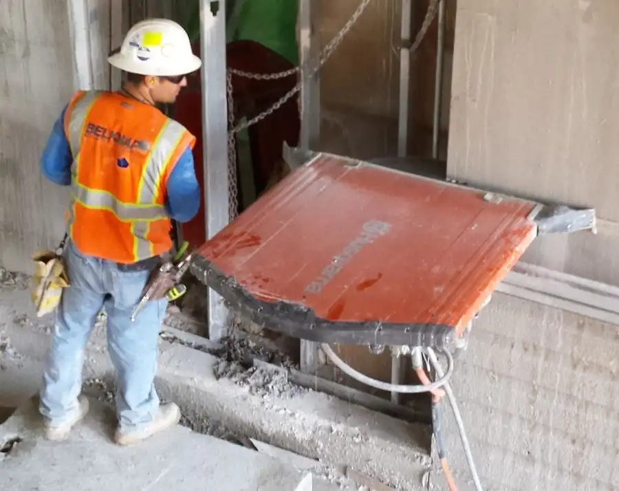 A Belknap technician in a branded hi-vis vest running a red wall saw head