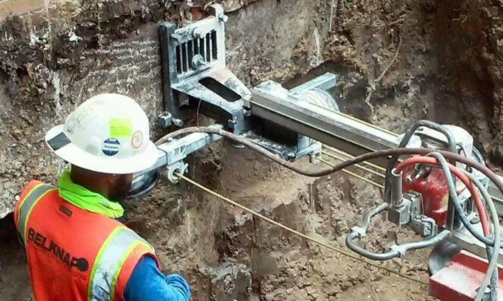 A Belknap technician setting a diamond wire-saw rig against a raw excavation face